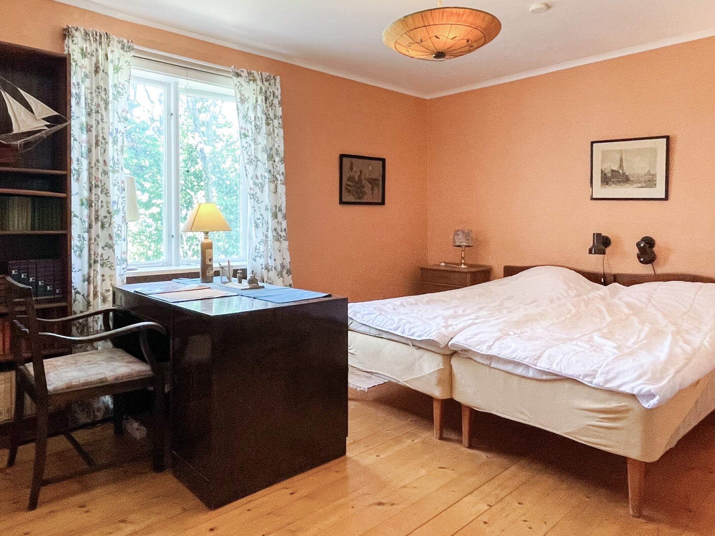 Un dormitorio con escritorio, silla, cama y ventana con cortinas.