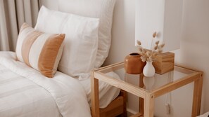 A neatly made bed with white and brown bedding, a small wooden nightstand with a vase and a cup, and a mirror on the wall. - The Coastal Oak - Pool | Linen and Towels | Pets | Wifi (Carrickalinga)