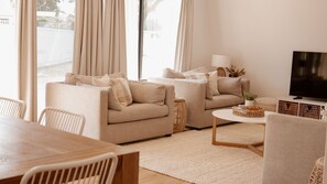 A living room with two sofas, a coffee table, a TV, and a dining area with chairs and a table. - The Coastal Oak - Pool | Linen and Towels | Pets | Wifi (Carrickalinga)