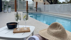 Ein Poolbereich mit Tisch, zwei Getränken, einer Snackschale und einem Strohhut.