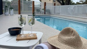 A poolside setting with a table, two drinks, a bowl of snacks, and a straw hat. - The Coastal Oak - Pool | Linen and Towels | Pets | Wifi (Carrickalinga)