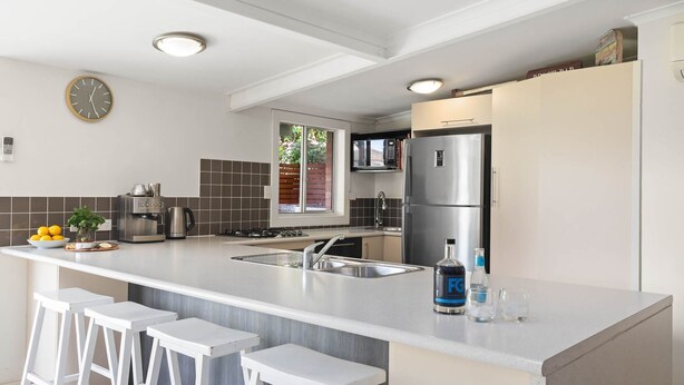 A modern kitchen with a central island, stainless steel appliances, and a clock on the wall. - The Anchorage - 1 Marjory Street (Normanville)