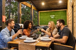 A group of people dining at an outdoor wooden table with a green wall in the background. - NEW! Pickleball, Hot Tub, ATV Trails, Outdoor Movies & Mini Golf (Broken Bow)
