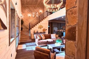 A spacious living area with a wooden staircase, a sofa set, and a dining table. - NEW! Pickleball, Hot Tub, ATV Trails, Outdoor Movies & Mini Golf (Broken Bow)
