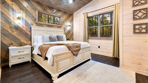 Ein Schlafzimmer mit einem großen Bett, Holzwänden, einem Deckenventilator und einem Fenster mit Vorhängen.