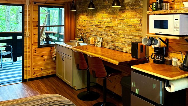 A rustic kitchen with wooden beams, a stone wall, and a bar area with stools.