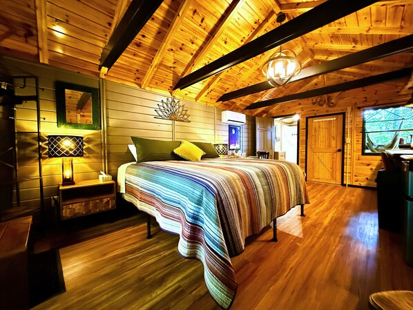 A wooden cabin interior with a bed, a nightstand, a lamp, a mirror, and a window. - The Roost, w/King bed and Mtn Views (Black Mountain)
