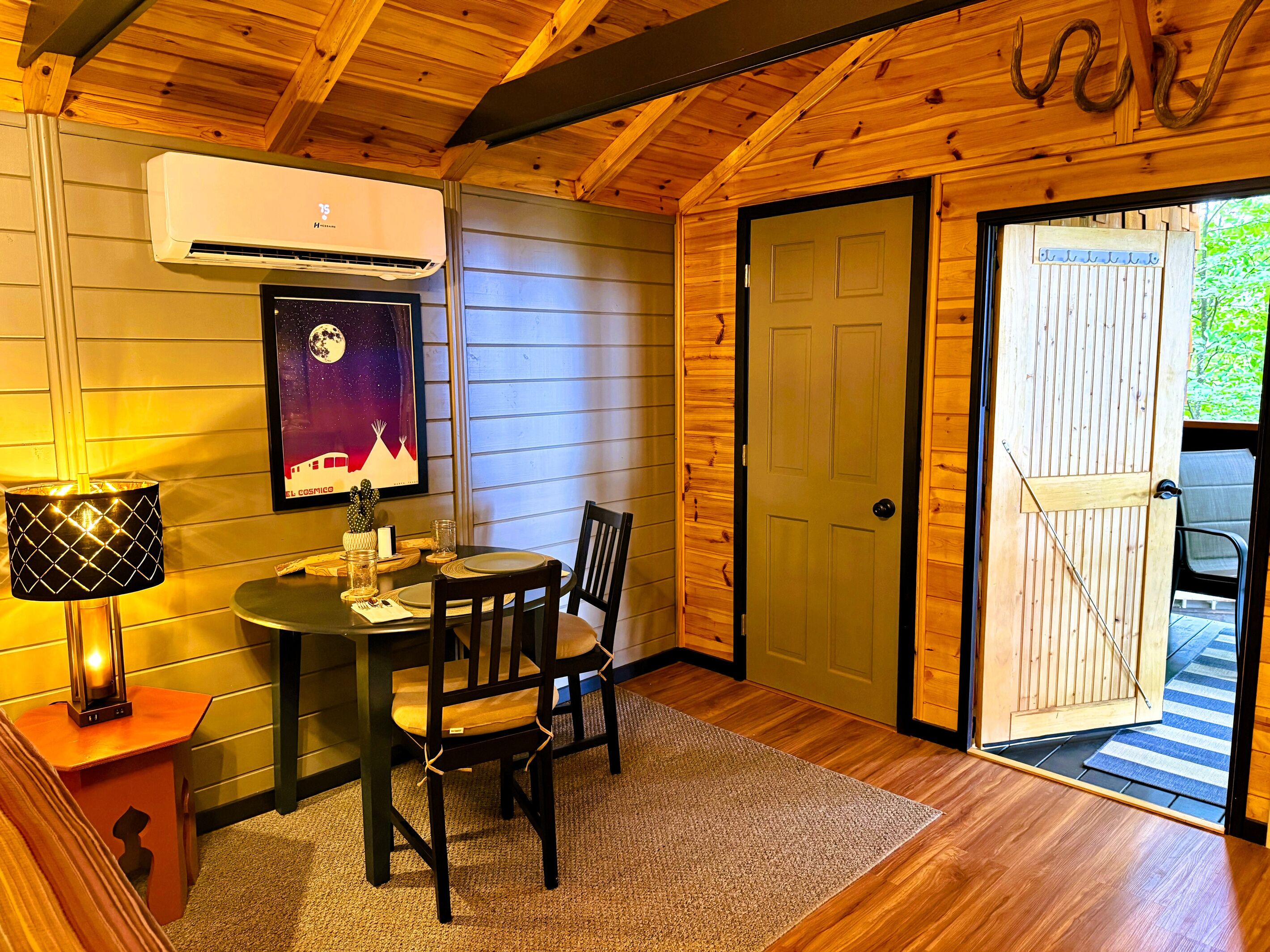 Ein Holzinterieur mit einem Esstisch, Stühlen, einer Lampe, einer Klimaanlage und einer Tür.