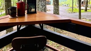 A wooden table with a red kettle and a cup, a chair, and a view of a forest and mountains through a window.