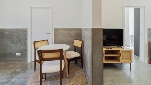 A room with a round table, two chairs, a television on a wooden stand, and a door. - Setúbal Downtown Fonte Nova, By Home Match (Setúbal)