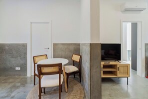 A room with a round table, two chairs, a television on a wooden stand, and a door. - Setúbal Downtown Fonte Nova, By Home Match (Setúbal)