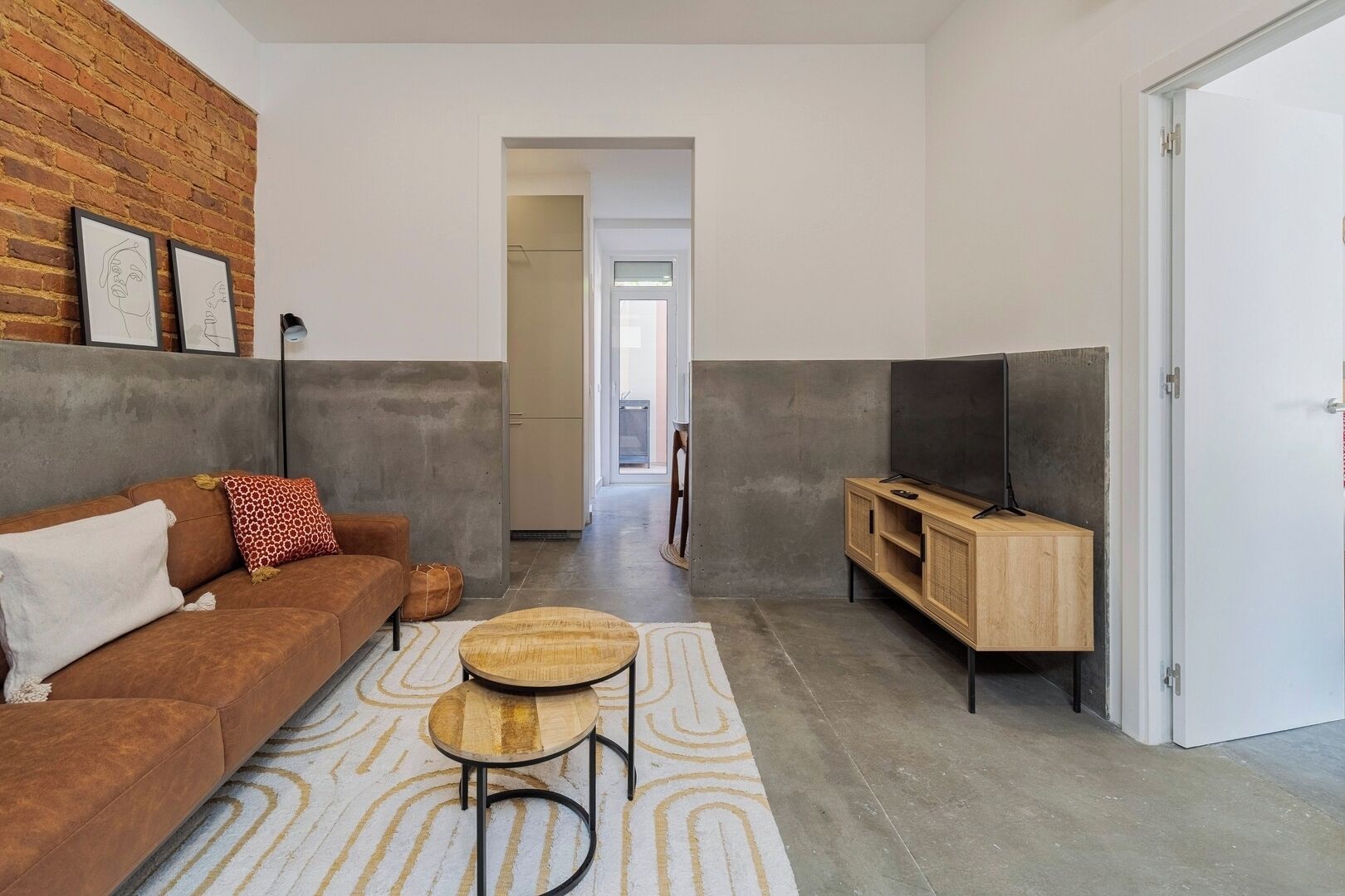 A modern living room with a sofa, a television on a wooden stand, a patterned rug, and a brick wall.