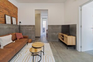 Un salon moderne avec un canapé, un téléviseur posé sur un meuble en bois, un tapis à motifs et un mur en briques.