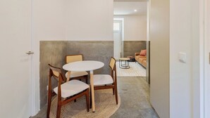A narrow hallway with a round table and chairs, a sofa with patterned cushions, and a door on the left. - Setúbal Downtown Fonte Nova, By Home Match (Setúbal)