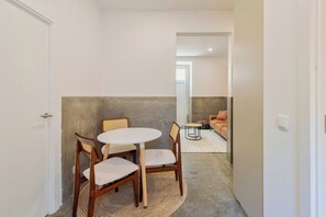 A narrow hallway with a round table and chairs, a sofa with patterned cushions, and a door on the left. - Setúbal Downtown Fonte Nova, By Home Match (Setúbal)