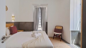 A bedroom with a bed, a chair, a window with curtains, and a wall-mounted light fixture. - Setúbal Downtown Fonte Nova, By Home Match (Setúbal)