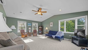 A living room with a ceiling fan, a sofa, a blue couch, a bookshelf, and a television.