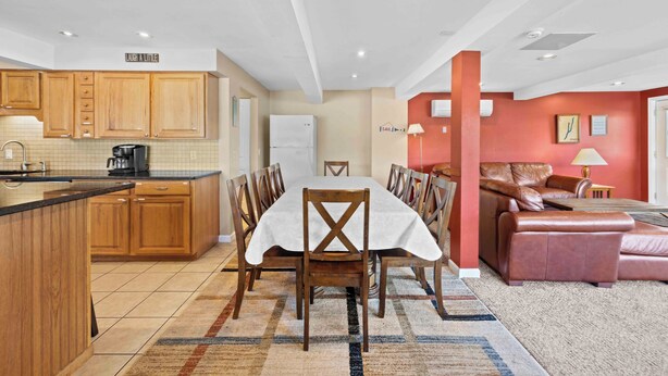 A modern kitchen with wooden cabinets, a dining table with chairs, a sofa, and a rug.