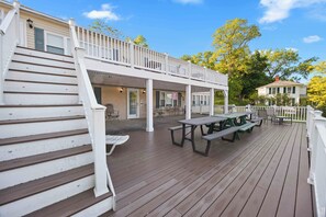 A wooden deck with picnic tables and chairs, a white railing, and a covered area with a door. - Waterfront Memories Begin at Deckside on Keuka! (Dundee)