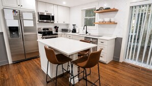 A modern kitchen with stainless steel appliances, a central island with bar stools, and a sliding glass door to the right.