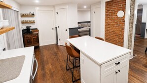 A compact kitchen with a dining area, wooden flooring, and a brick accent wall.