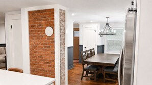 A modern kitchen with a brick accent wall, a dining area with a wooden table and chairs, and a stainless steel refrigerator.