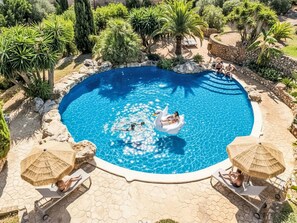 Ein Swimmingpool mit einem Schwaneinhorn-Schwimmspielzeug, umgeben von Palmen und einer Steinmauer.