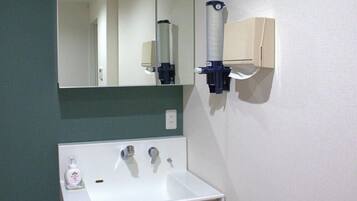 Un baño con un lavamanos blanco, un espejo, un secador de manos y un dispensador de jabón.