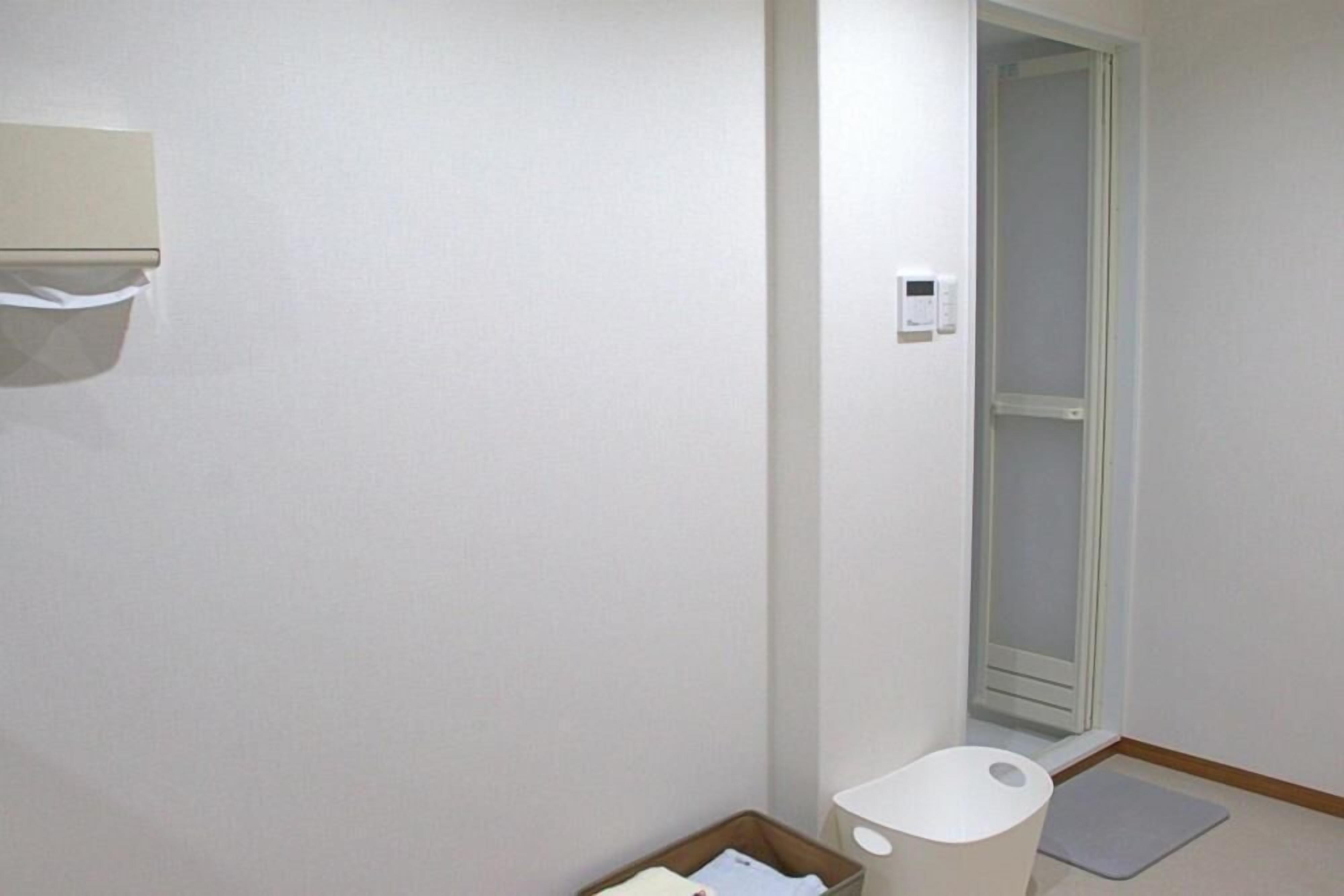 Un baño con inodoro, un cubo de basura, un pequeño espacio de almacenamiento y zona de ducha.