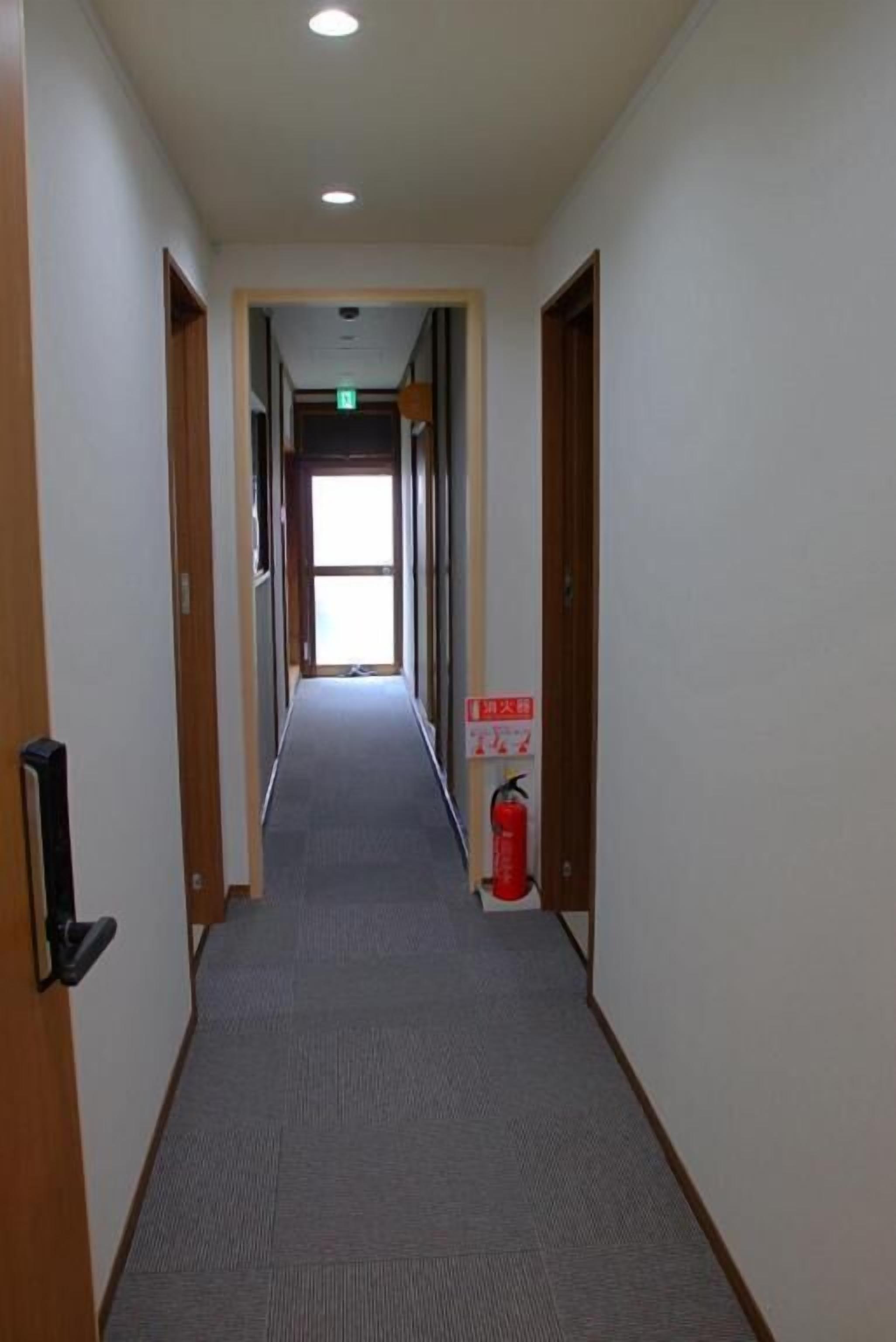 Un pasillo con puertas de madera, un extintor y un cartel con texto en japonés.