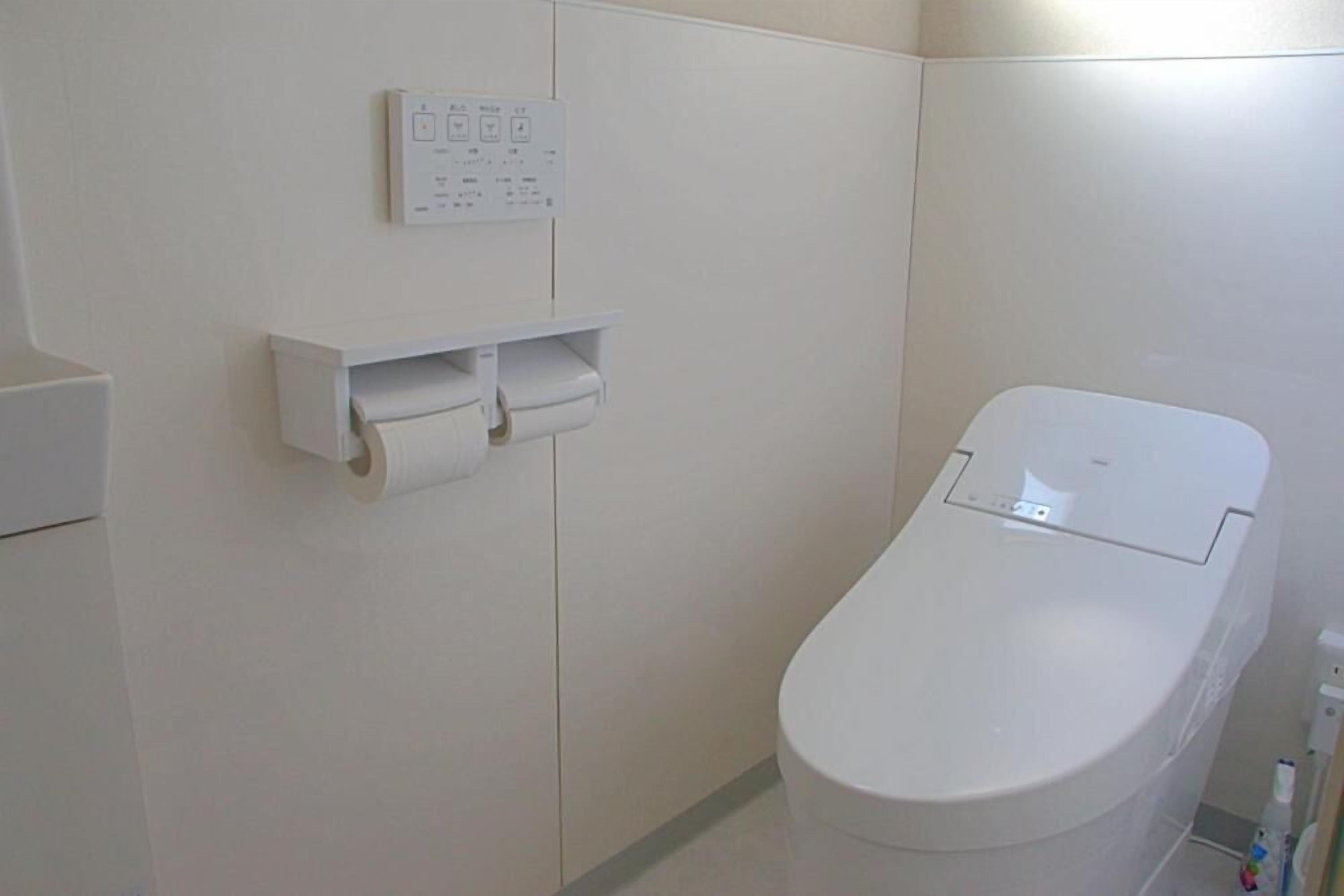 A toilet with a white tank and a wall-mounted paper towel dispenser.