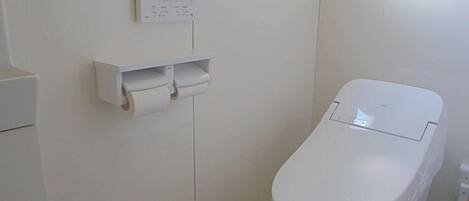Inodoro con tanque blanco y dispensador de toallas de papel instalado en la pared.