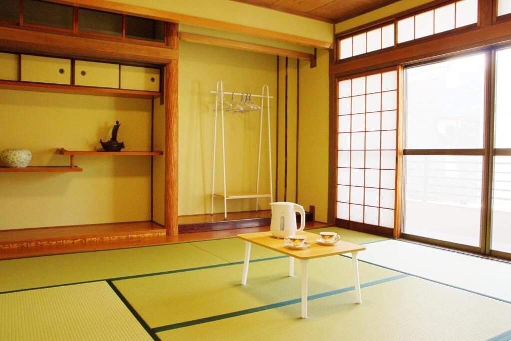 Une pièce de style japonais traditionnel, avec un sol recouvert de tatamis, un paravent shoji, un service à thé posé sur une petite table et un porte-vêtements suspendu.
