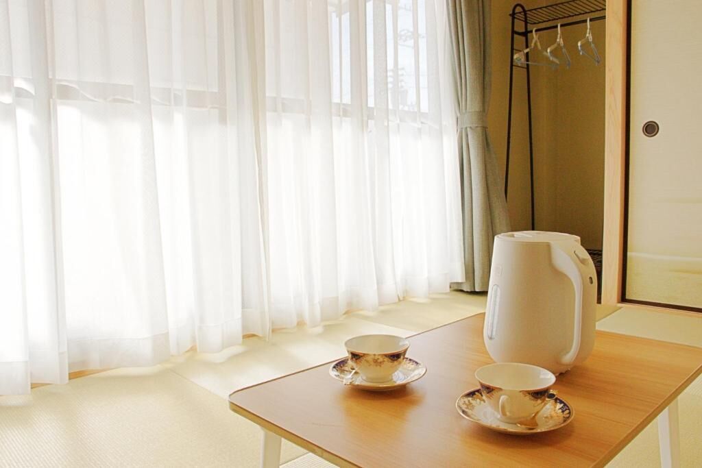 A room with a wooden table, two cups, a teapot, and a window with sheer curtains.
