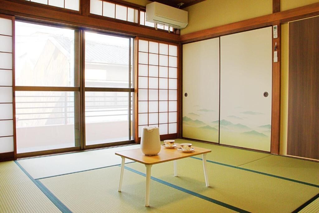 A traditional Japanese room with tatami flooring, sliding doors, and a table with a vase and cups.