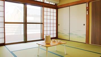 A traditional Japanese room with tatami flooring, sliding doors, and a table with a vase and cups.