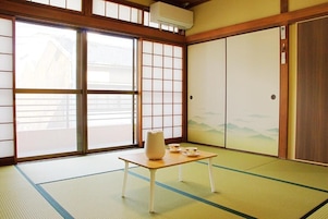 Una habitación japonesa tradicional con suelo de tatami, puertas correderas y una mesa con un florero y tazas.