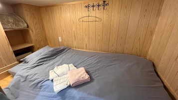 Una habitación con cama, paredes de madera, un estante y un perchero.