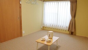A room with a wooden door, a window with curtains, a small table with a kettle and cups, and a carpeted floor. - Shimanami Guest House Orangenokaze - Hostel  (Imabari)
