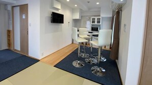 A modern hotel room with a kitchenette, a dining area with bar stools, and a TV mounted on the wall. - Shimanami Guest House Orangenokaze - Hostel  (Imabari)