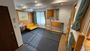 A compact room with a bunk bed, a sofa, a desk, and a painting on the wall.