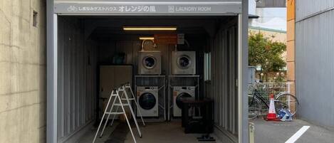 A laundry room with multiple washing machines, a ladder, and a bicycle outside.