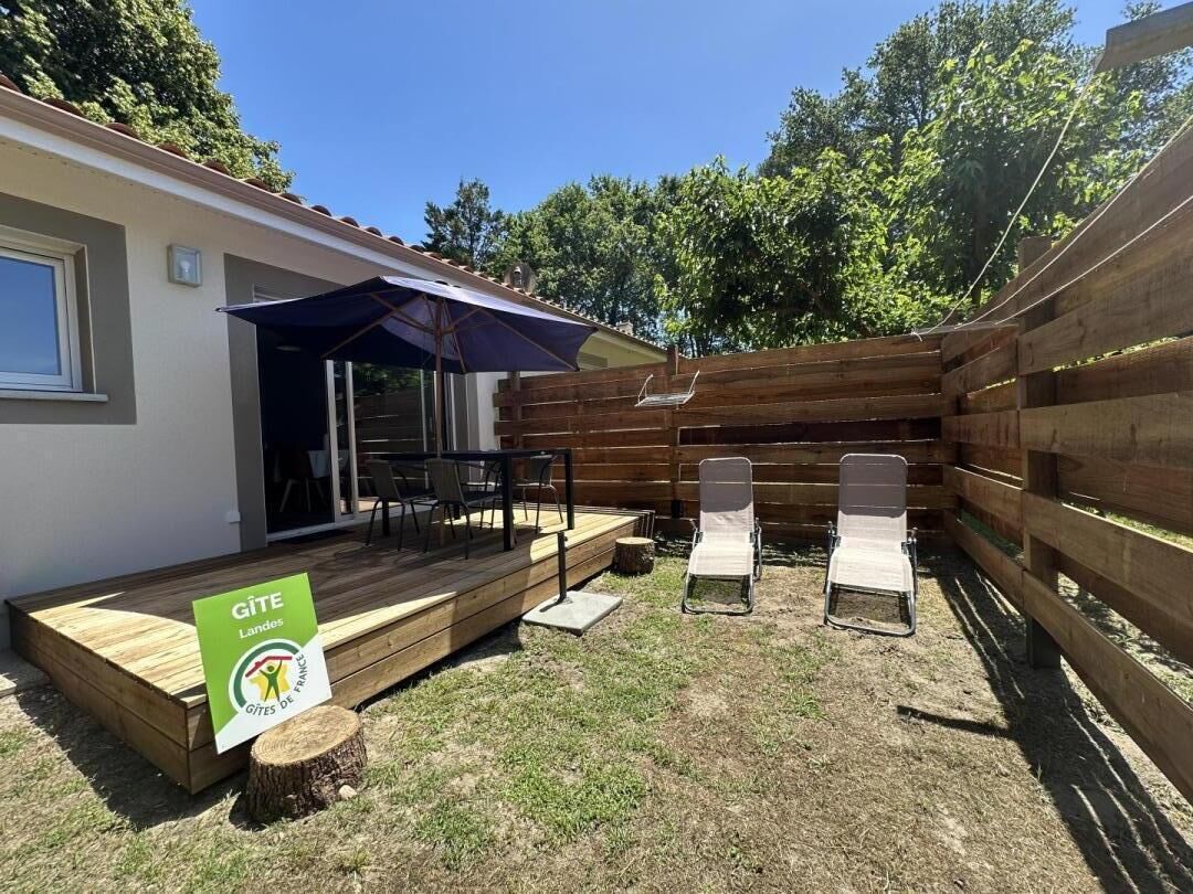 Un patio con terraza de madera, una mesa, dos sillones de descanso y un cartel que indica que es un Gîte en Francia.