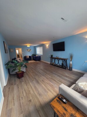 A living room with a wooden floor, a sofa, a coffee table, and a TV mounted on the wall. - Casa Azul : Cozy Retreat Near Obama Library (Chicago)