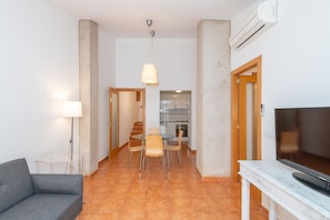 A living room with a sofa, a dining table with chairs, a TV, and a kitchen in the background. - Apartment with parking in downtown Begur (Begur)