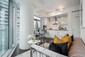 Een moderne keuken met witte kastjes, een eethoek met een ronde tafel en stoelen, en een groot raam met uitzicht op de stad.