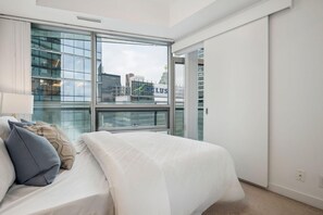 Een moderne hotelkamer met een groot raam, een bed met witte beddengoed en uitzicht op de stad.