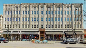A large, historic building with a symmetrical facade, multiple storefronts at the ground level, and a central entrance with a decorative archway. - Cozy 1-bedroom condo in downtown Louisville with free parking and gym access (Louisville)