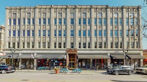 Ein großes, historisches Gebäude mit einer symmetrischen Fassade, mehreren Geschäften im Erdgeschoss und einem zentralen Eingang mit einem verzierten Bogen.