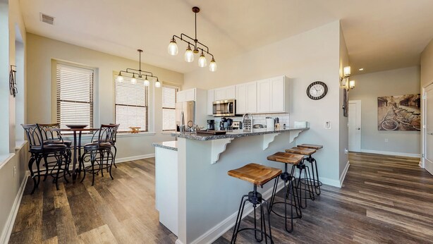 A modern kitchen with a central island, bar stools, and a dining area with chairs. - Cozy 1-bedroom condo in downtown Louisville with free parking and gym access (Louisville)